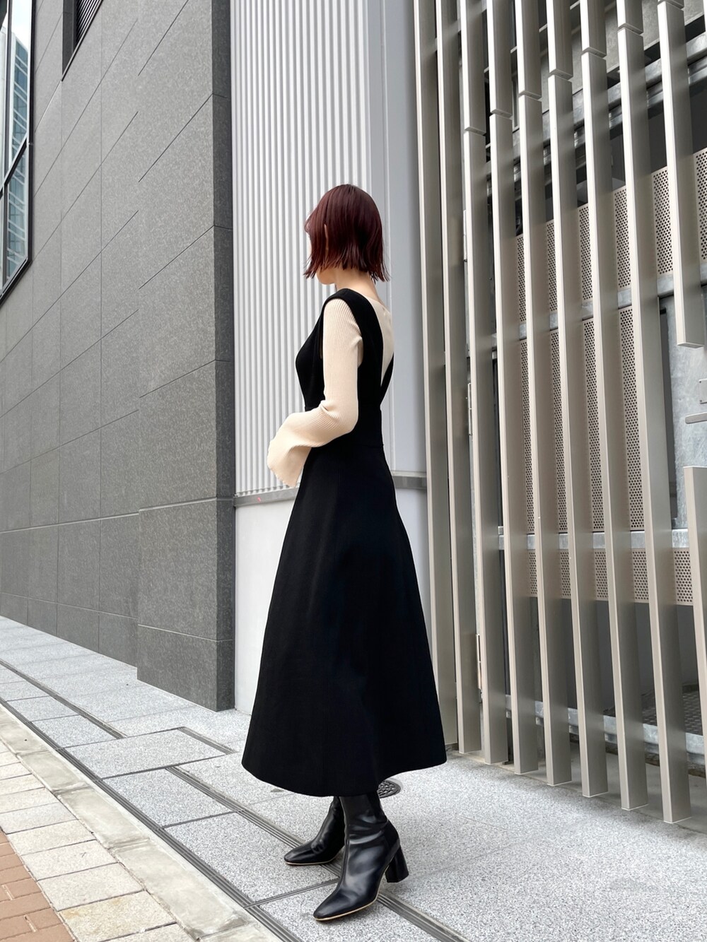 ホワイト系のニット/セーター、ブラック系のジャンパースカート、ブラック系のブーツを着用したレディースの冬コーディネートの2枚目の写真