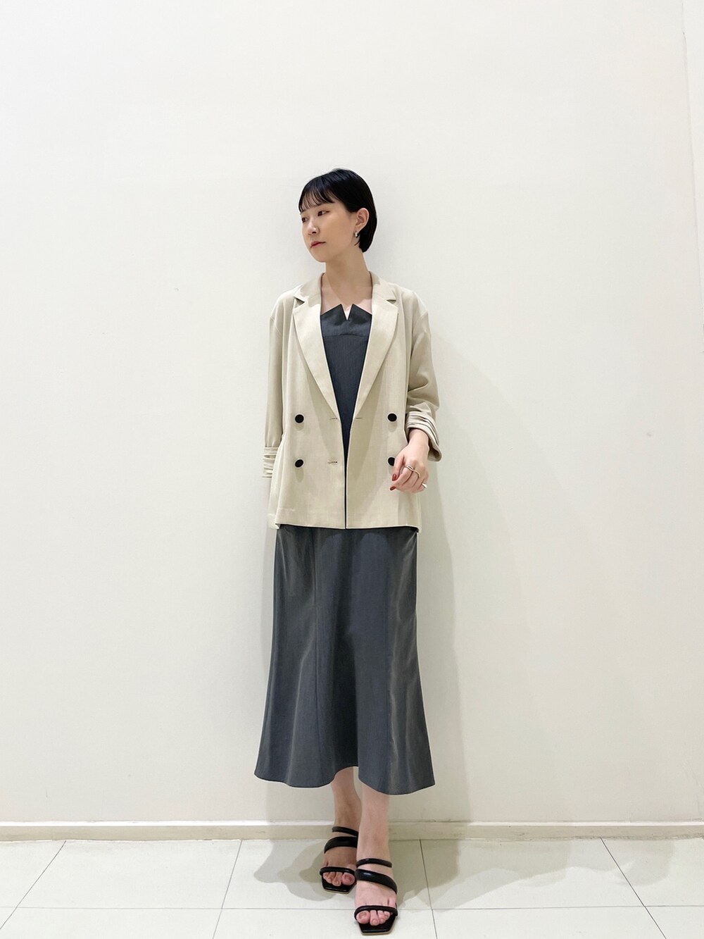 ベージュ系のテーラードジャケット、グレー系のワンピース、ブラック系のサンダルを着用したレディースの春コーディネートの2枚目の写真