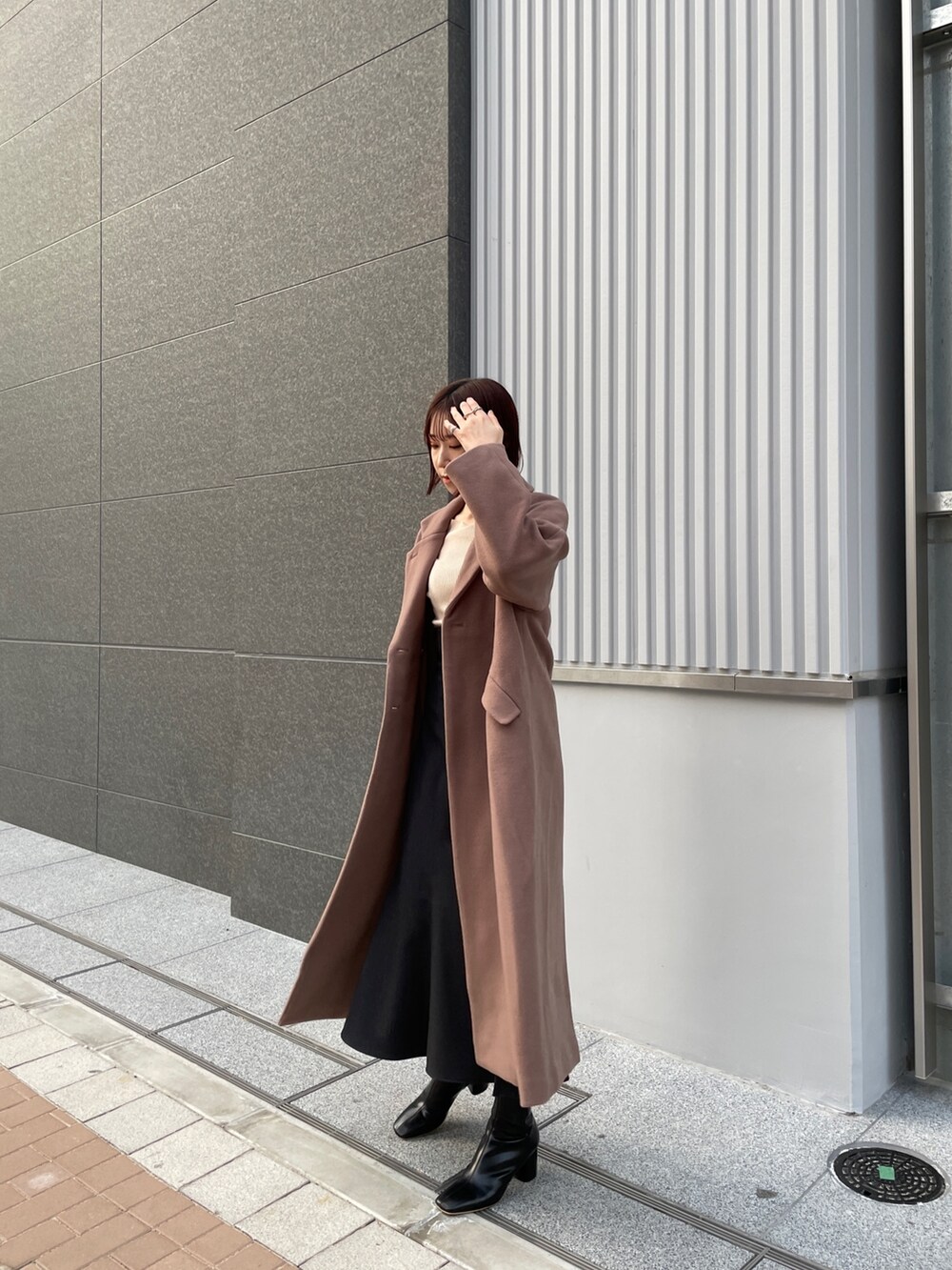 ブラウン系のチェスターコート、ホワイト系のニット/セーター、グレー系のスカートを着用したレディースの冬コーディネートの2枚目の写真