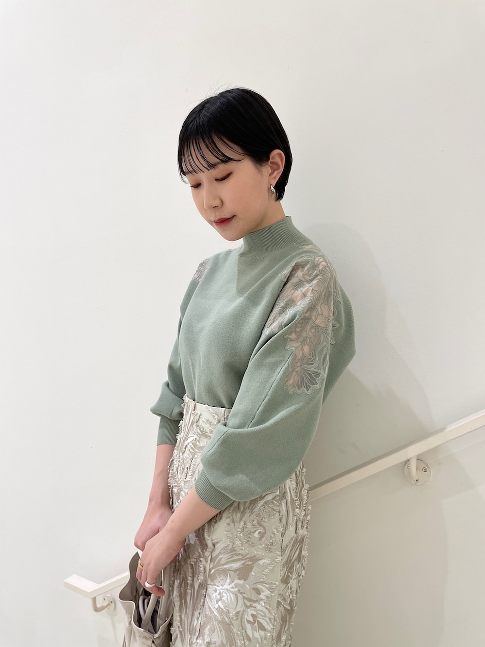 ベージュ系のスカート、グリーン系のニット/セーター、ホワイト系のハンドバッグを着用したレディースの冬コーディネートの5枚目の写真