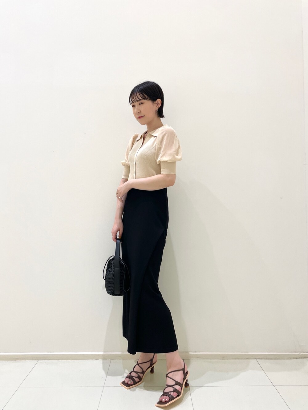 ブラック系のスカート、ホワイト系のニット/セーター、ブラック系のハンドバッグを着用したレディースの夏コーディネートの2枚目の写真
