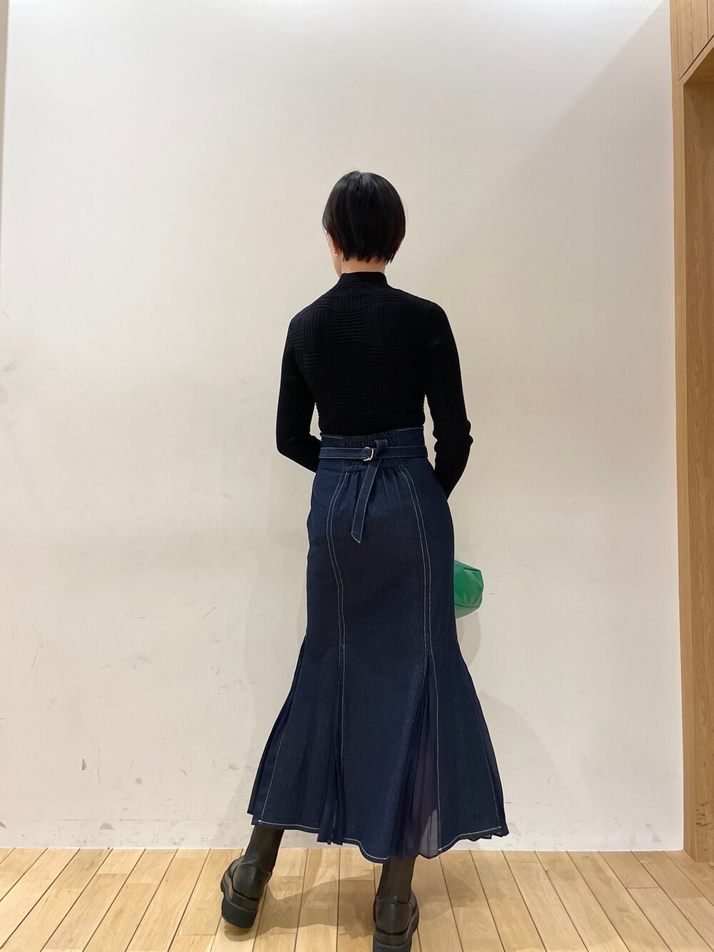 ブルー系のスカート、ブラック系のニット/セーター、グリーン系のハンドバッグを着用したレディースの冬コーディネートの4枚目の写真