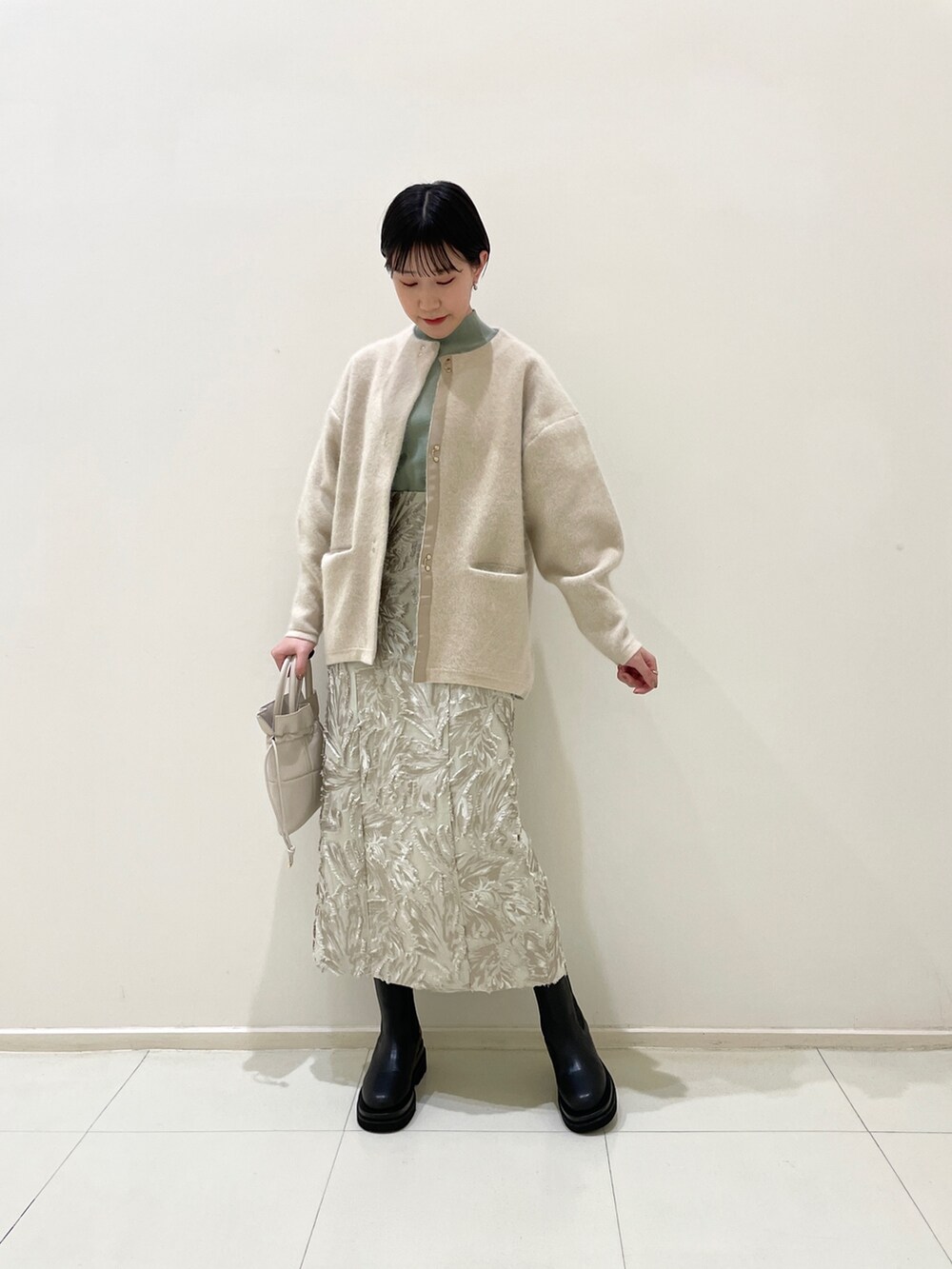 ベージュ系のスカート、グリーン系のニット/セーター、ホワイト系のハンドバッグを着用したレディースの冬コーディネートの8枚目の写真