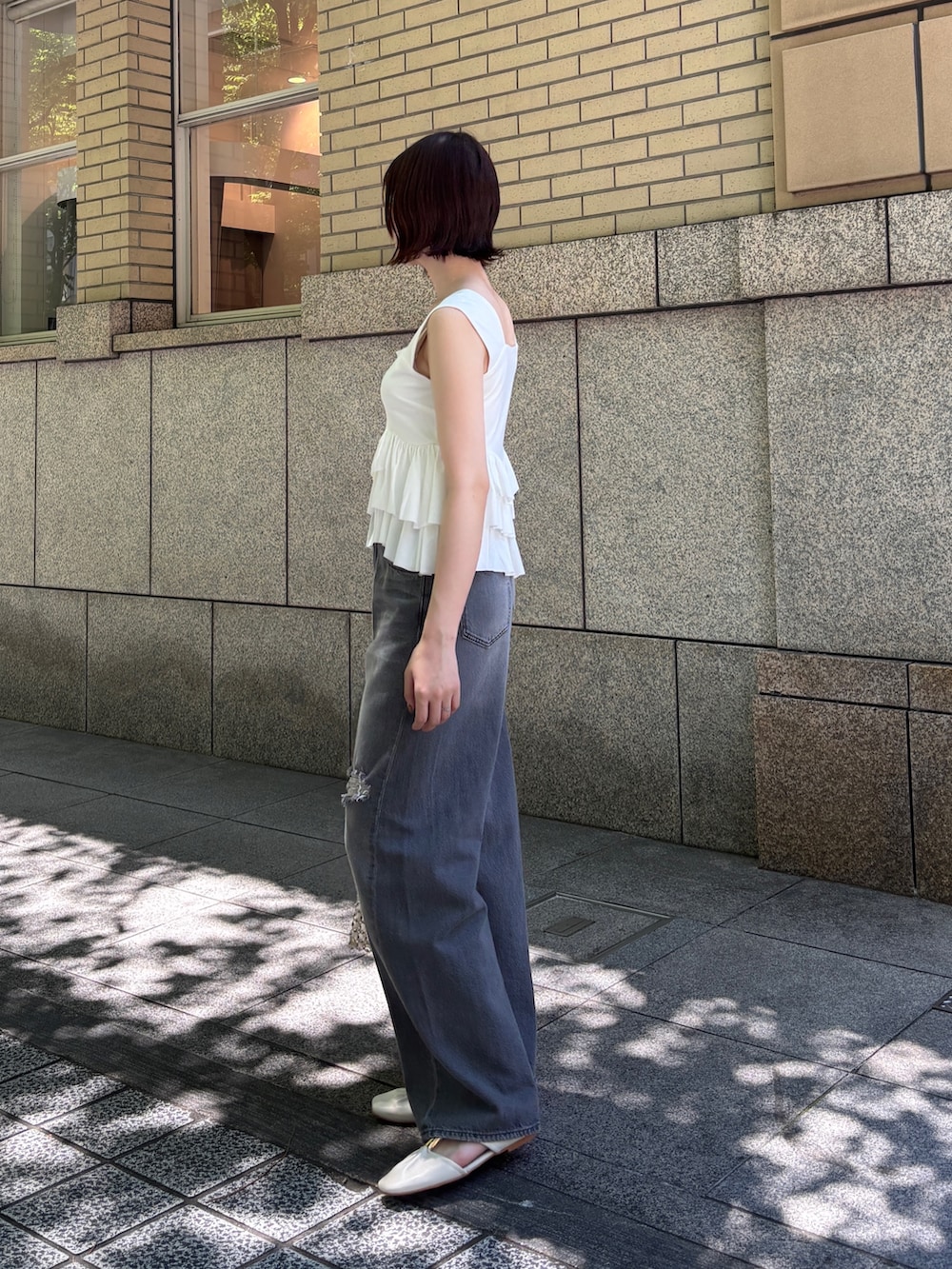 グレー系のデニムパンツ、ホワイト系のハンドバッグ、ホワイト系のサンダルを着用したレディースの春コーディネートの2枚目の写真