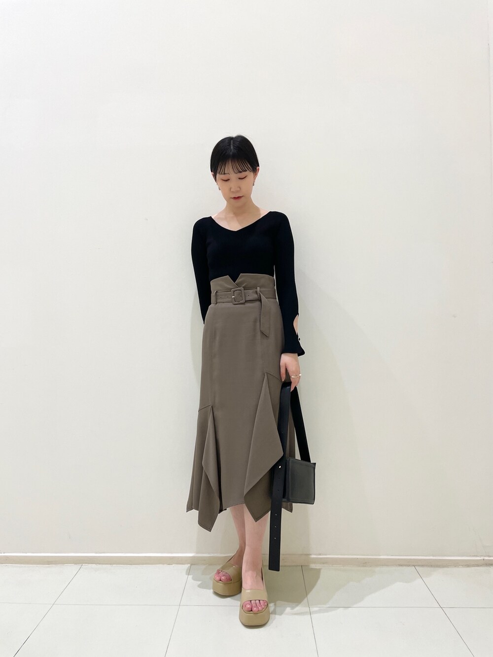 ブラウン系のスカート、ブラック系のニット/セーター、ベージュ系のサンダルを着用したレディースの春コーディネートの3枚目の写真