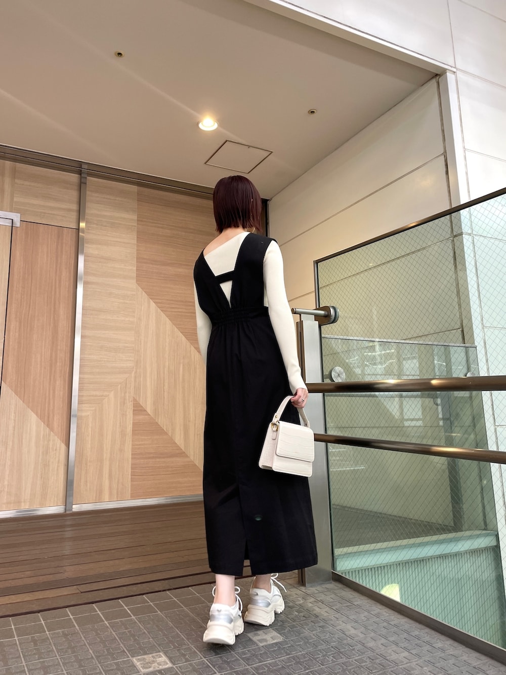 ブラック系のジャンパースカート、ホワイト系のショルダーバッグ、ホワイト系のニット/セーターを着用したレディースの春コーディネートの3枚目の写真