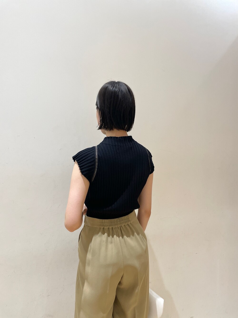 ブラック系のニット/セーター、ベージュ系のスラックス、ホワイト系のハンドバッグを着用したレディースの夏コーディネートの7枚目の写真