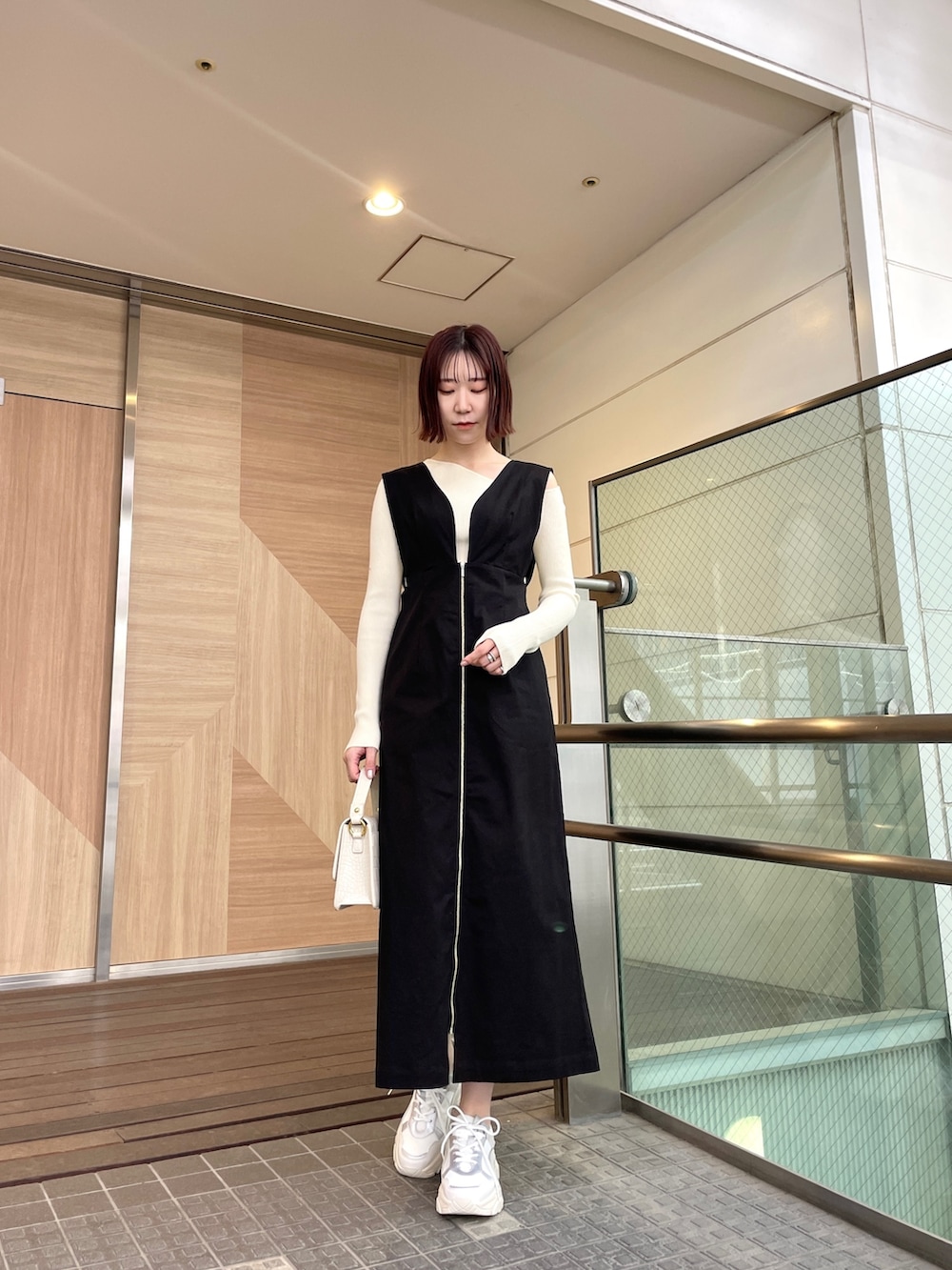 ブラック系のジャンパースカート、ホワイト系のショルダーバッグ、ホワイト系のニット/セーターを着用したレディースの春コーディネートの2枚目の写真