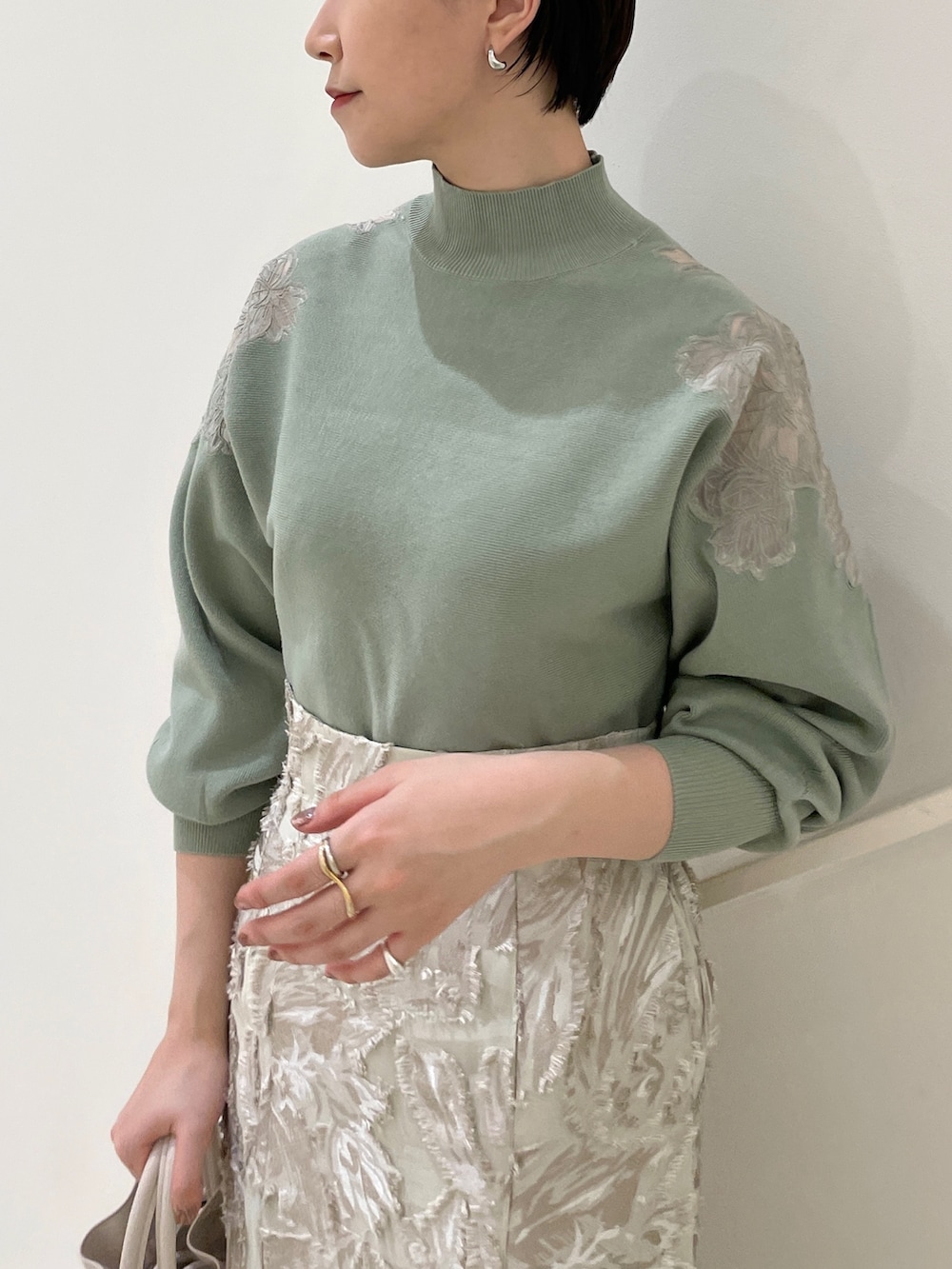 ベージュ系のスカート、グリーン系のニット/セーター、ホワイト系のハンドバッグを着用したレディースの冬コーディネートの6枚目の写真