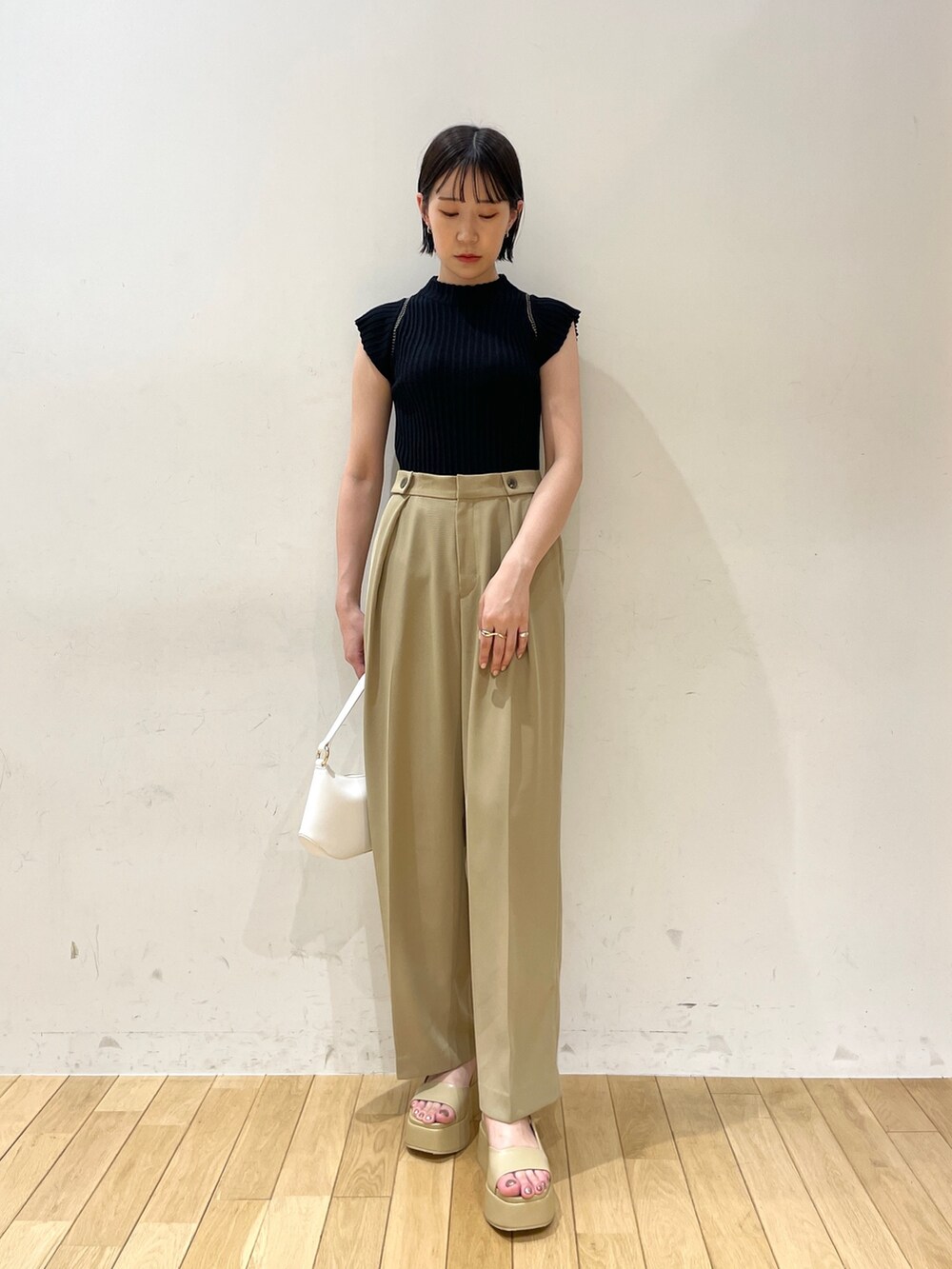 ブラック系のニット/セーター、ベージュ系のスラックス、ホワイト系のハンドバッグを着用したレディースの夏コーディネートの2枚目の写真