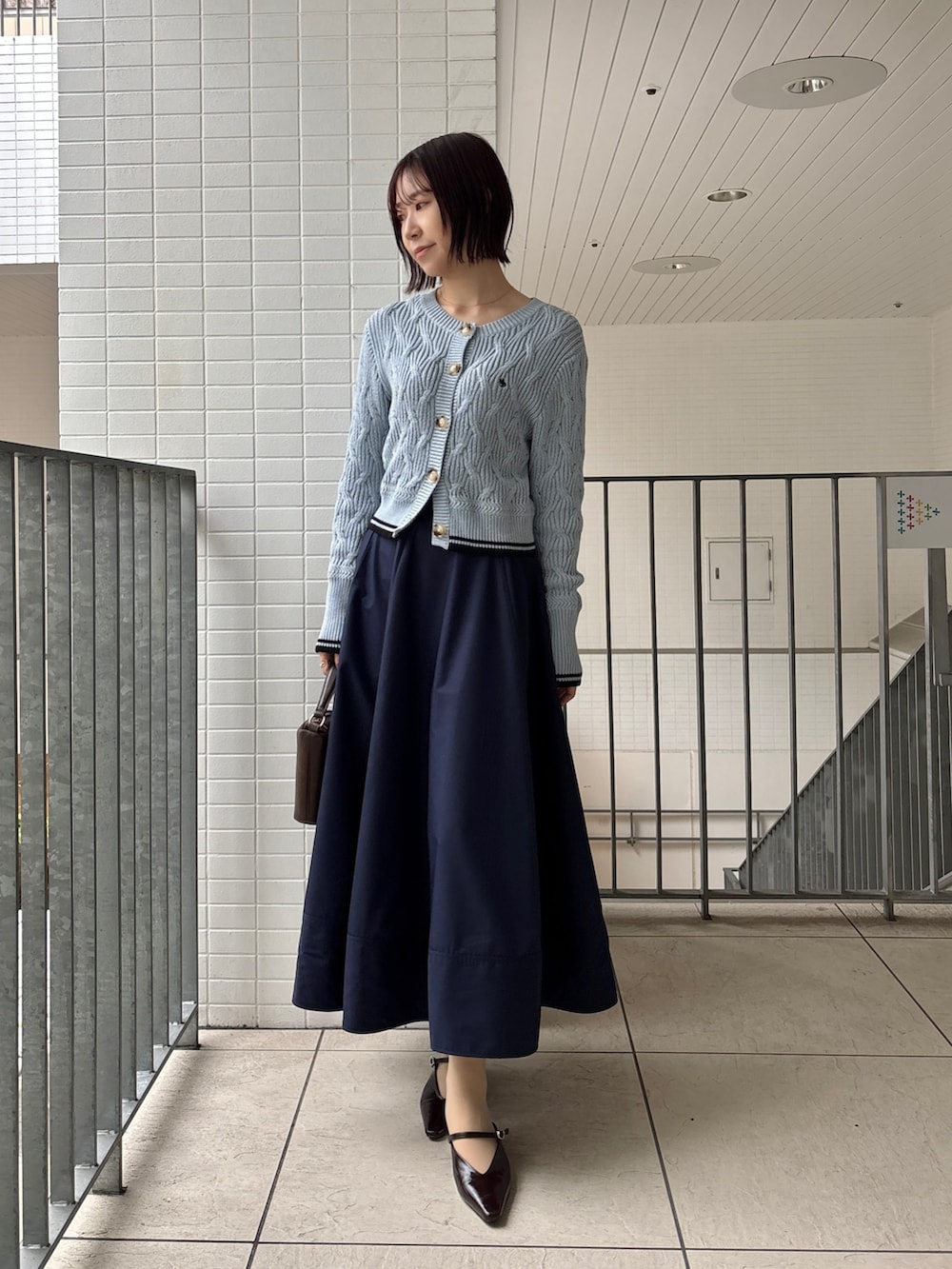 ブルー系のスカート、ブルー系のワンピース、ブラウン系のハンドバッグを着用したレディースの春コーディネートの2枚目の写真