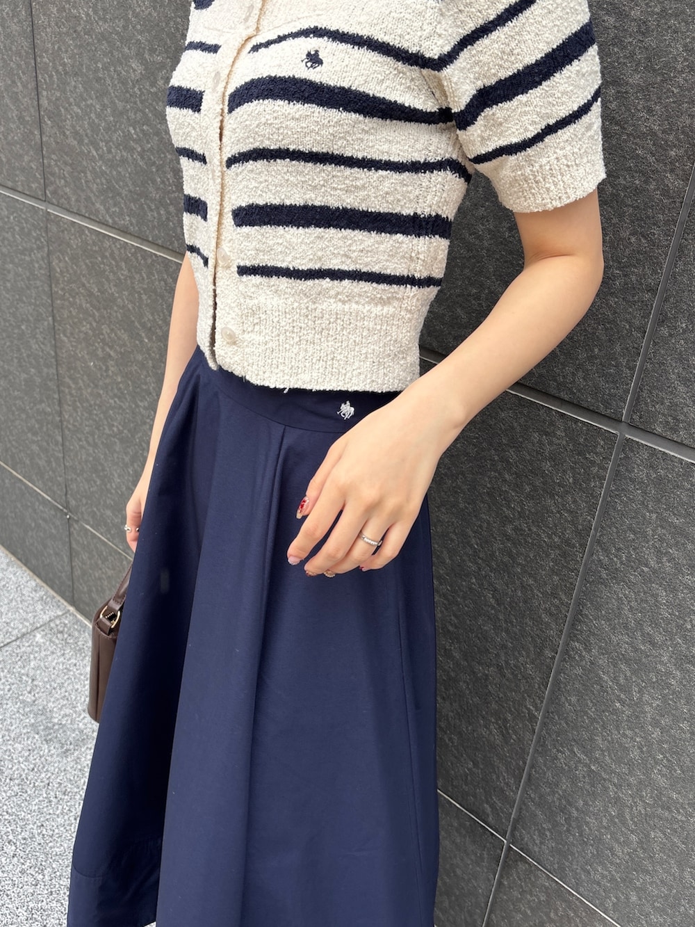 ブルー系のスカート、ホワイト系のニット/セーター、ブラウン系のハンドバッグを着用したレディースの春コーディネートの6枚目の写真