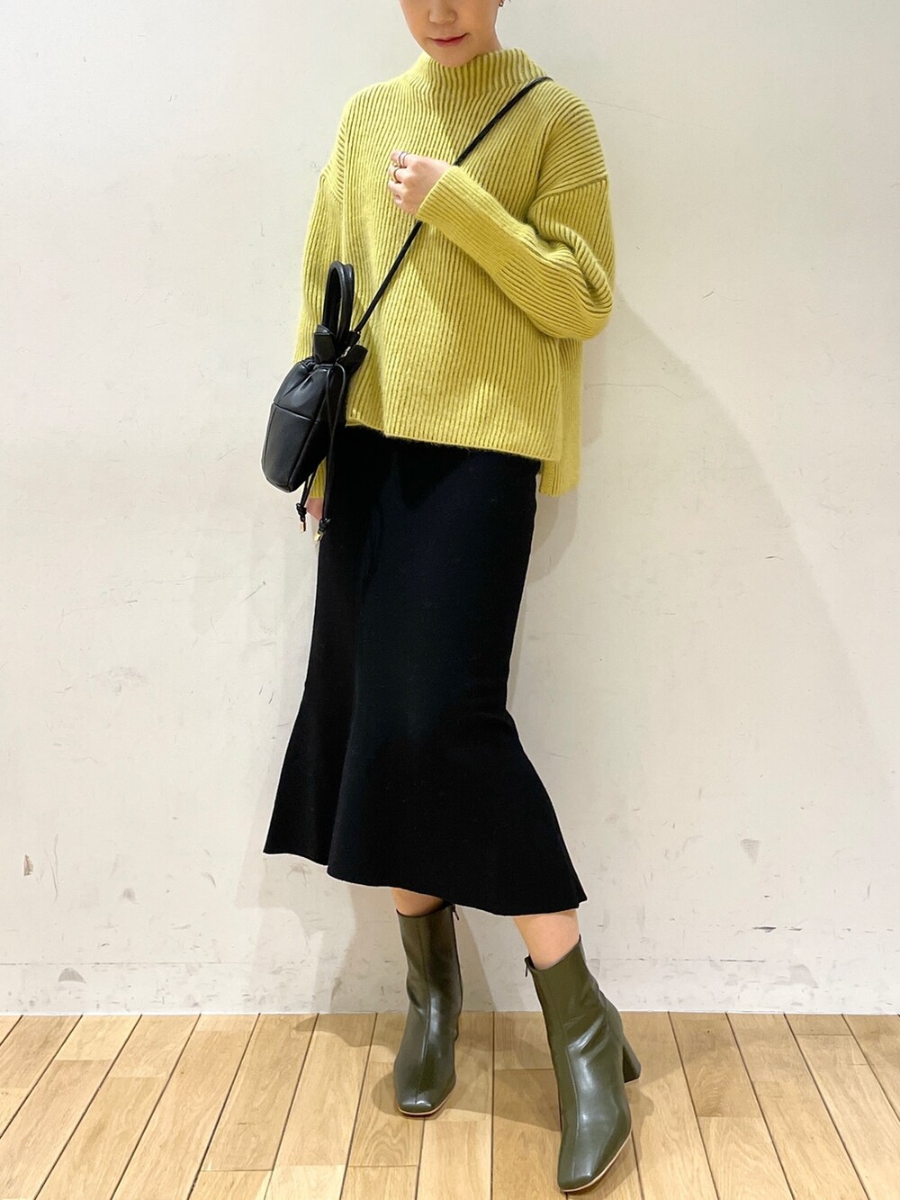 イエロー系のニット/セーター、ブラック系のスカート、ブラック系のハンドバッグを着用したレディースの冬コーディネートの2枚目の写真