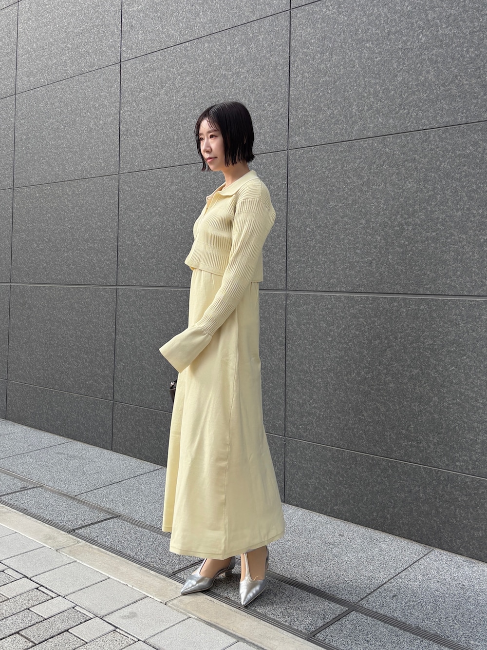 イエロー系のワンピース、ブラウン系のハンドバッグ、シルバー系のパンプスを着用したレディースの冬コーディネートの2枚目の写真