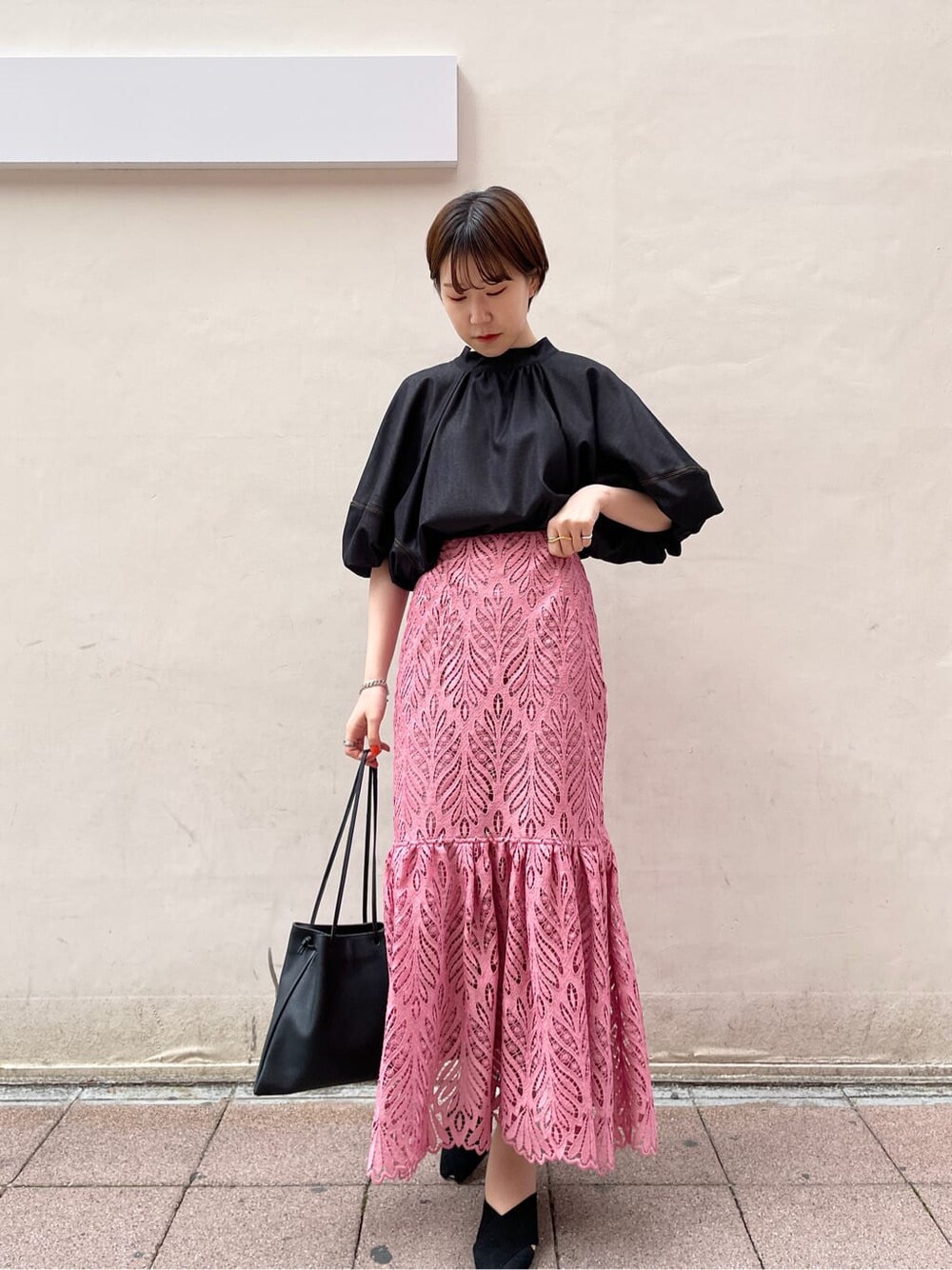 ブラック系のハンドバッグ、ブラック系のサンダル、ピンク系のスカートを着用したレディースの春コーディネートの2枚目の写真