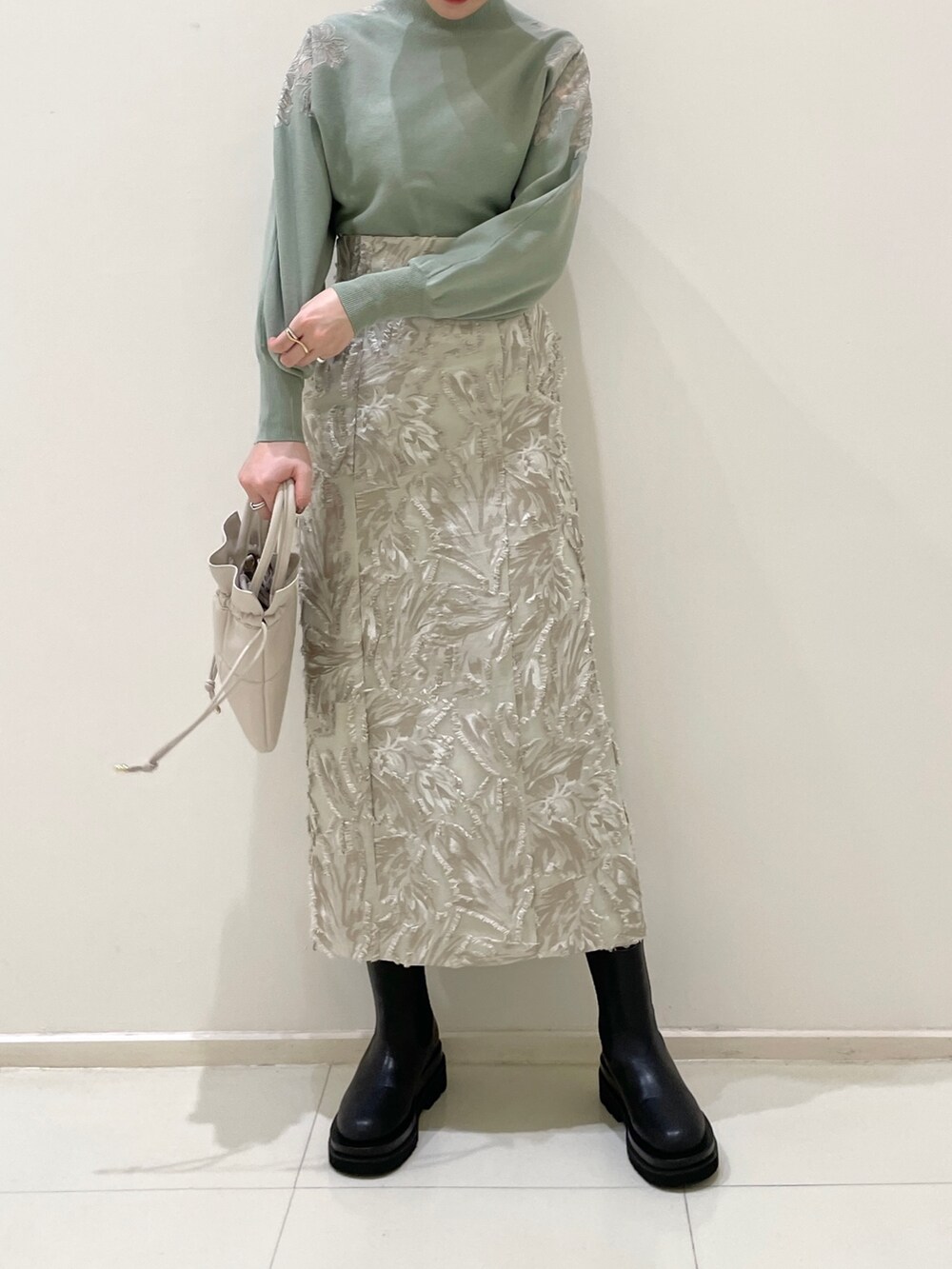 ベージュ系のスカート、グリーン系のニット/セーター、ホワイト系のハンドバッグを着用したレディースの冬コーディネートの4枚目の写真