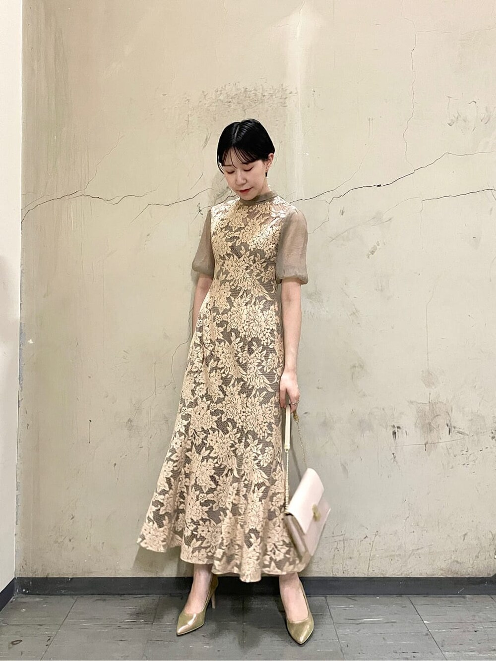 ベージュ系のドレス、ゴールド系のパンプス、ベージュ系のクラッチバッグを着用したレディースの秋コーディネートの2枚目の写真