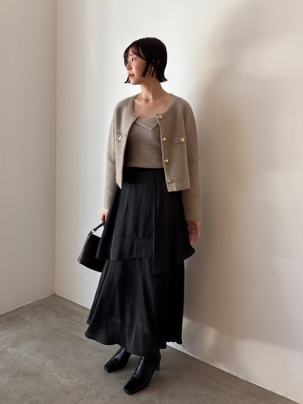 ブラック系のブーツ、ブラウン系のハンドバッグ、ブラック系のスカートを着用したレディースの秋コーディネートの2枚目の写真