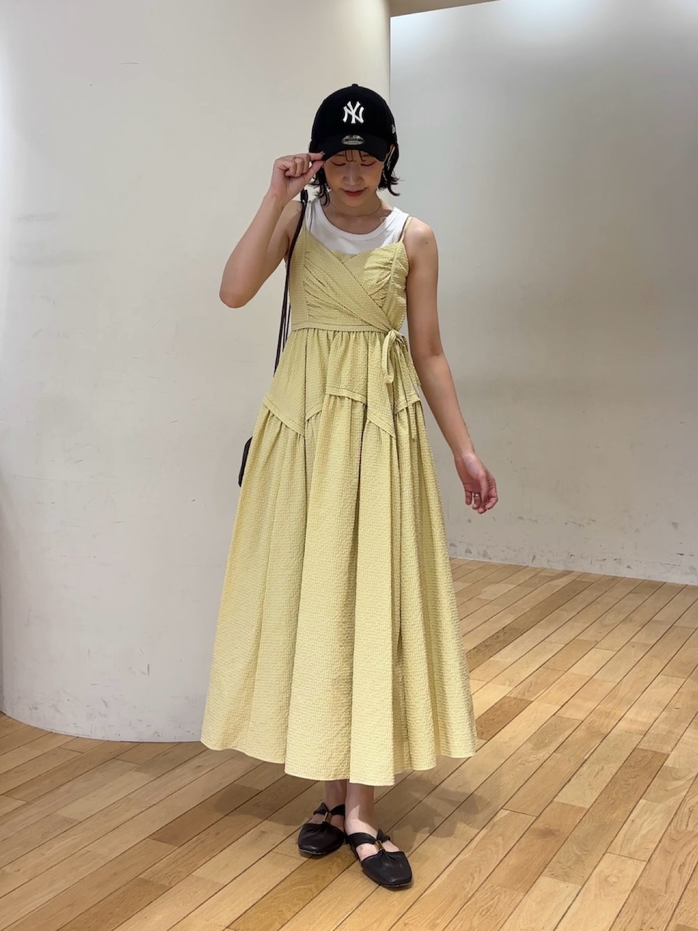 イエロー系のワンピース、ホワイト系のタンクトップ、ブラウン系のハンドバッグを着用したレディースの夏コーディネートの2枚目の写真