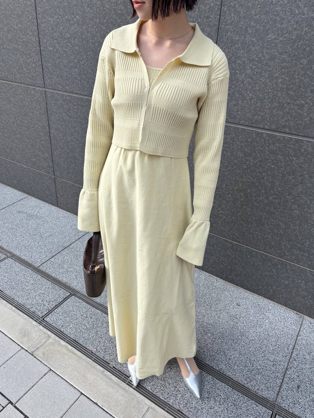 イエロー系のワンピース、ブラウン系のハンドバッグ、シルバー系のパンプスを着用したレディースの冬コーディネートの4枚目の写真