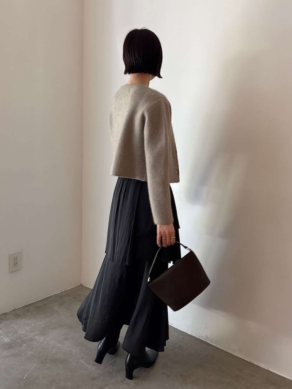 ブラック系のブーツ、ブラウン系のハンドバッグ、ブラック系のスカートを着用したレディースの秋コーディネートの3枚目の写真