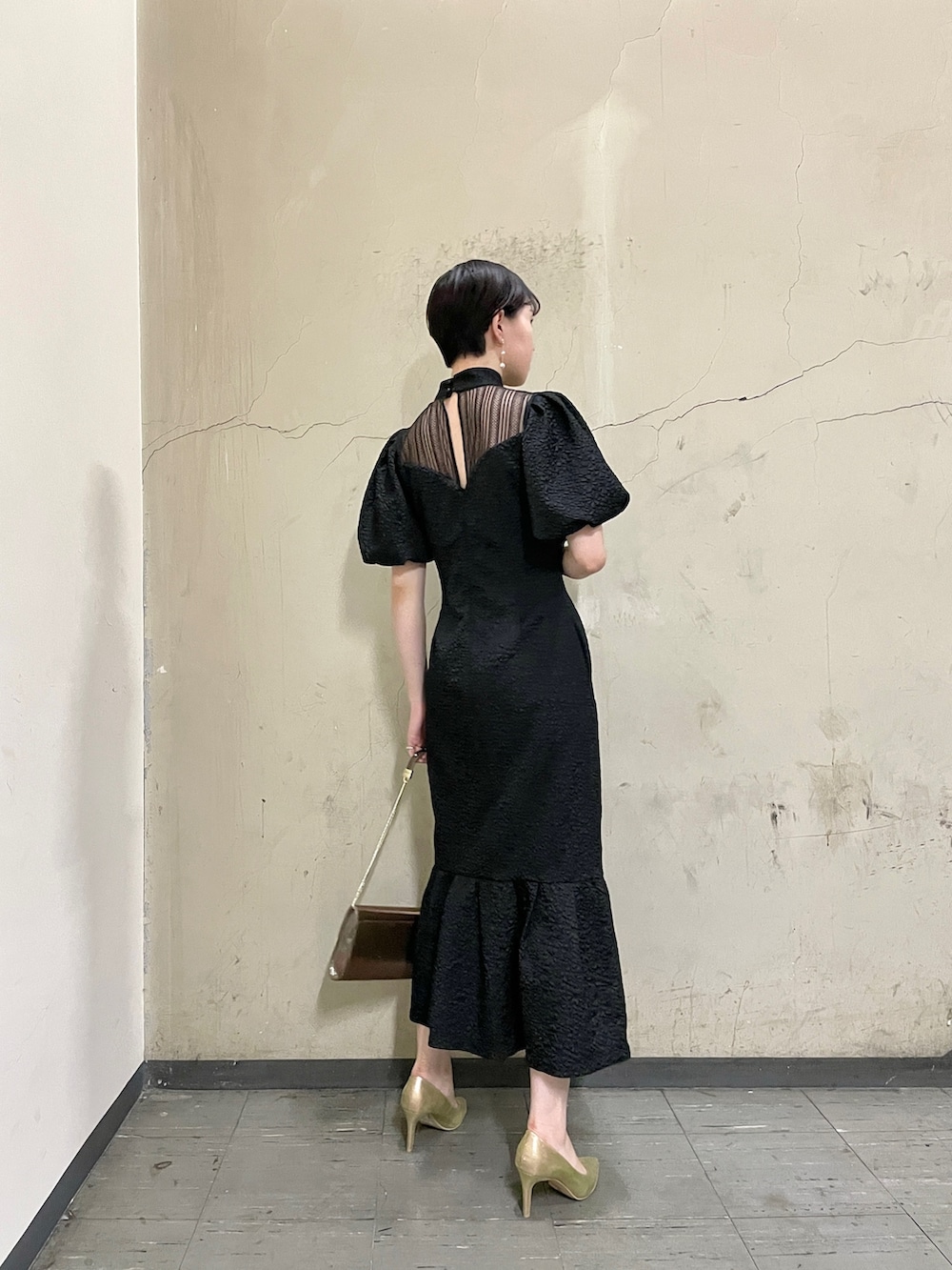 ブラック系のドレス、ゴールド系のハンドバッグ、ゴールド系のパンプスを着用したレディースの秋コーディネートの4枚目の写真