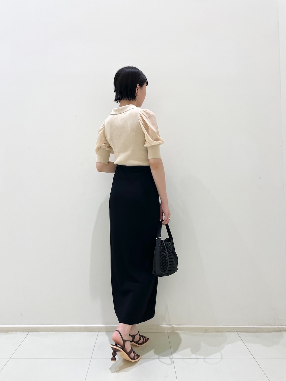 ブラック系のスカート、ホワイト系のニット/セーター、ブラック系のハンドバッグを着用したレディースの夏コーディネートの4枚目の写真