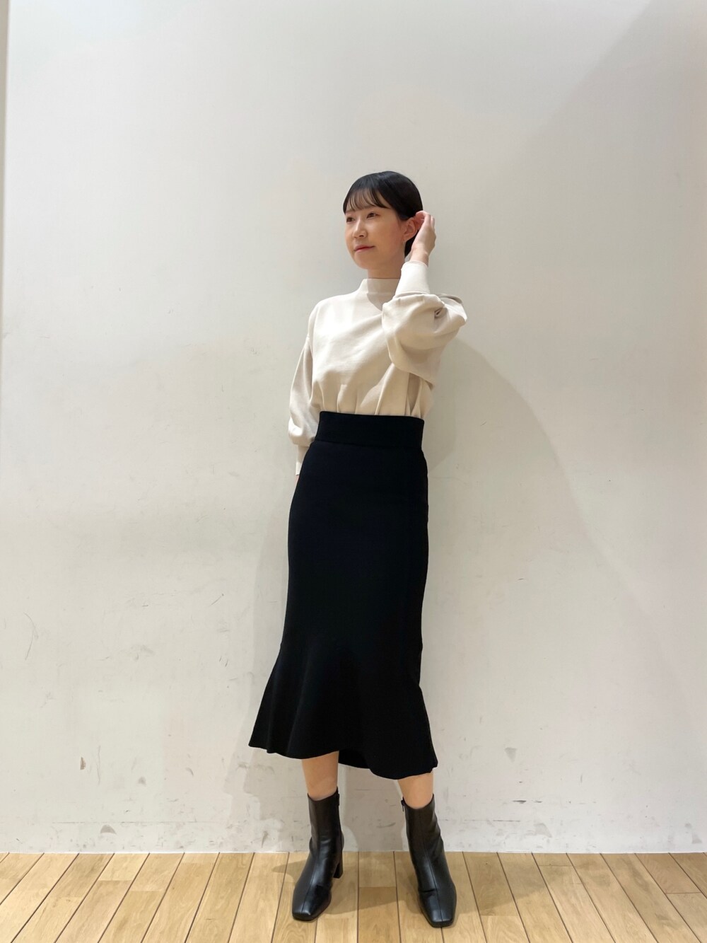 ブラック系のスカート、ホワイト系のニット/セーター、ブラック系のブーツを着用したレディースの冬コーディネートの2枚目の写真