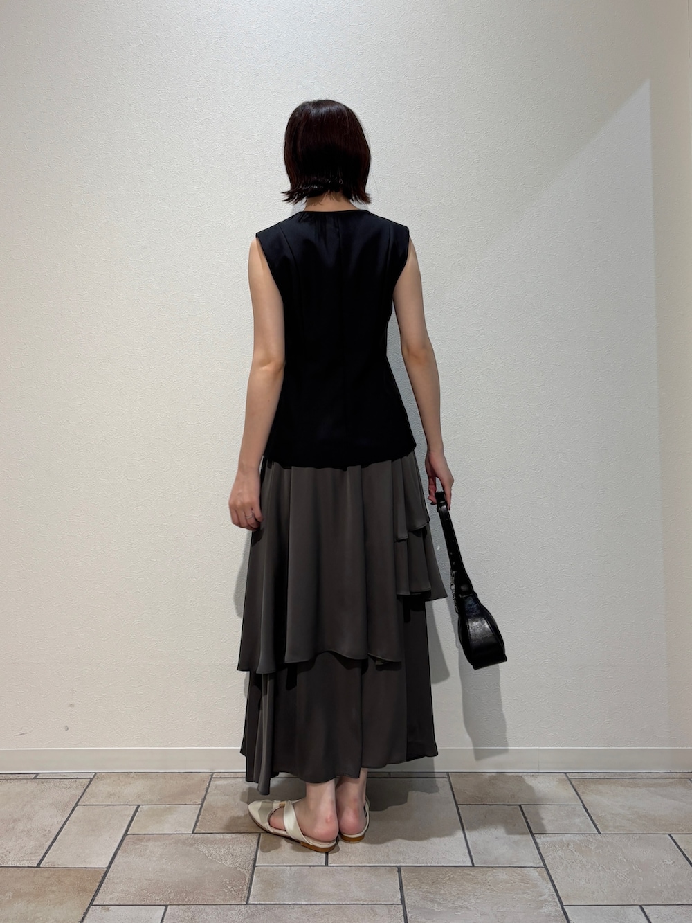 ブラック系のワンピース、ブラック系のハンドバッグ、ホワイト系のサンダルを着用したレディースの夏コーディネートの3枚目の写真