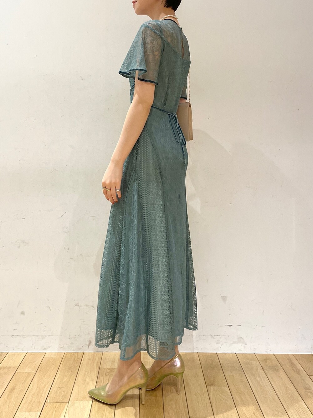 グリーン系のドレス、ベージュ系のクラッチバッグ、ゴールド系のパンプスを着用したレディースの冬コーディネートの4枚目の写真