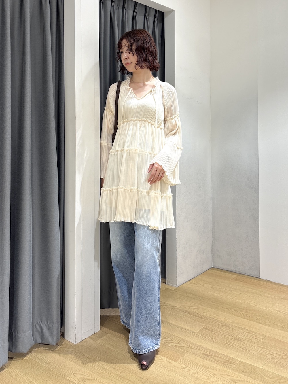 ホワイト系のワンピース、ブルー系のデニムパンツ、ブラウン系のハンドバッグを着用したレディースの秋コーディネートの2枚目の写真