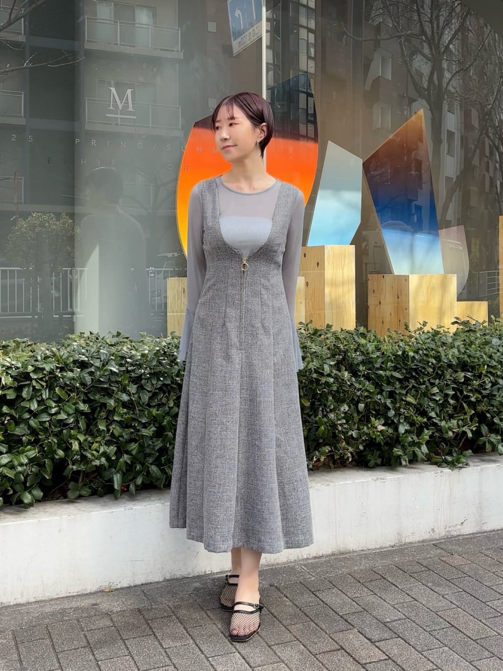 グレー系のジャンパースカート、ブルー系のTシャツ/カットソー、ブラック系のサンダルを着用したレディースの春コーディネートの2枚目の写真