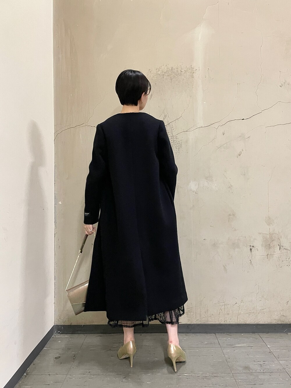 ブラック系のノーカラーコート、ブラック系のドレス、ゴールド系のハンドバッグを着用したレディースの秋コーディネートの3枚目の写真