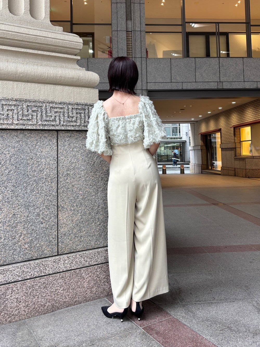 グリーン系のパンツドレス、ブラック系のパンプス、ブラック系のハンドバッグを着用したレディースの冬コーディネートの3枚目の写真