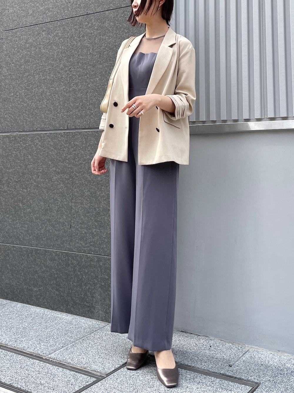 グレー系のパンツドレス、その他のパンプス、ベージュ系のテーラードジャケットを着用したレディースの春コーディネートの2枚目の写真