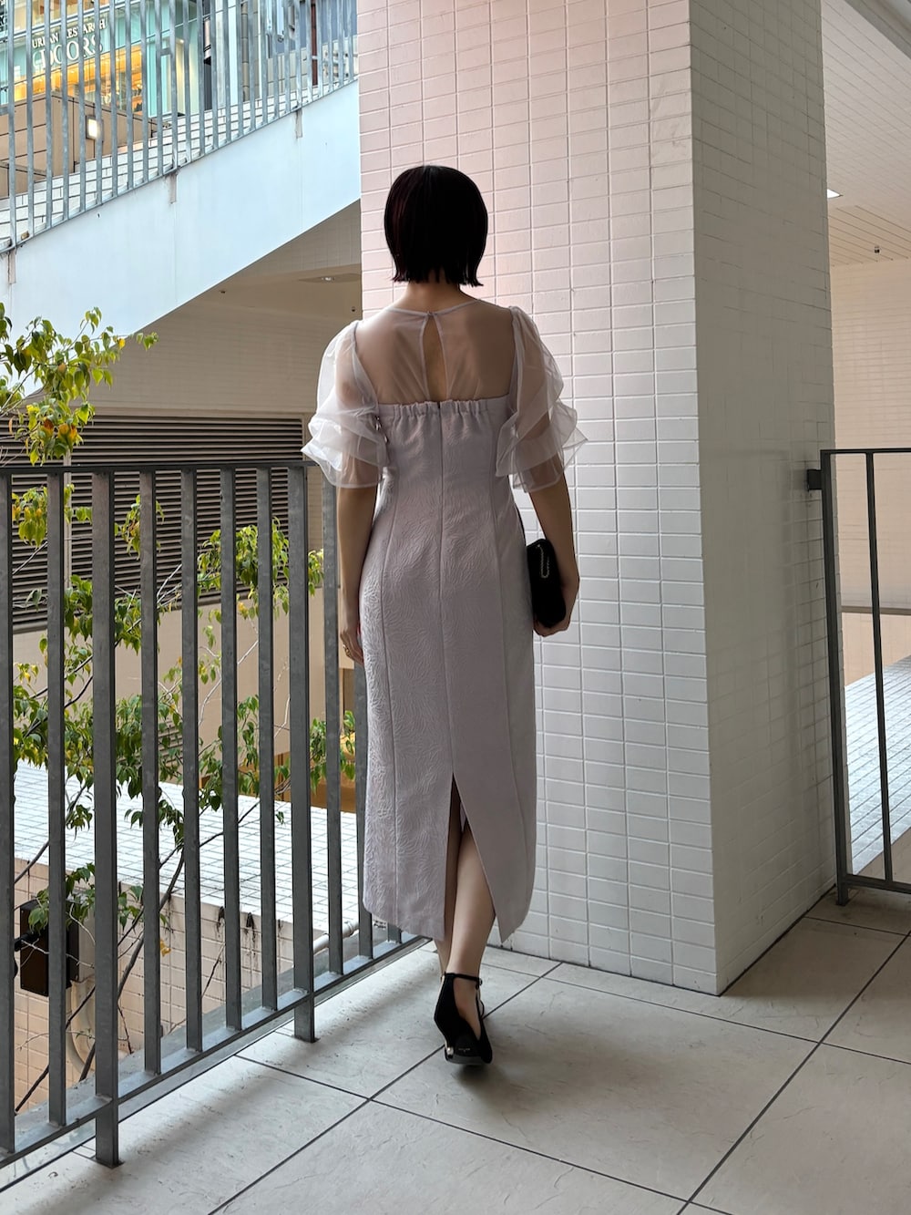 パープル系のドレス、ブラック系のハンドバッグ、ブラック系のパンプスを着用したレディースの冬コーディネートの3枚目の写真