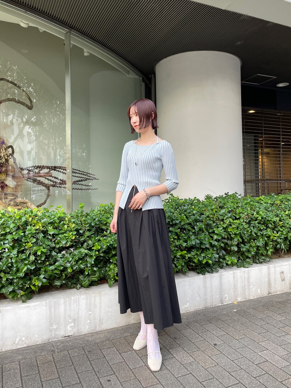 ブラック系のスカート、ブルー系のニット/セーター、ホワイト系のパンプスを着用したレディースの春コーディネートの2枚目の写真