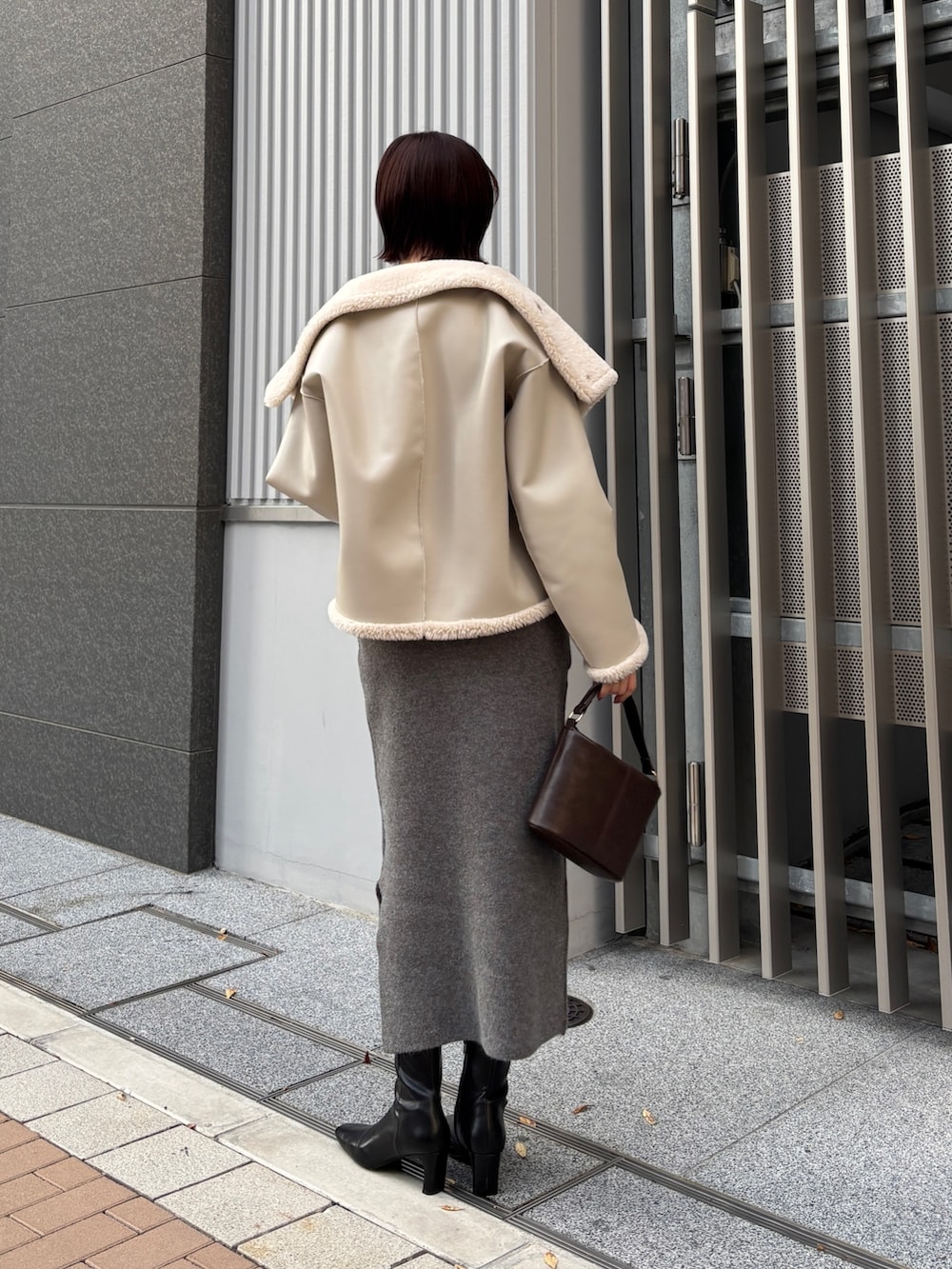 グレー系のワンピース、ブラウン系のハンドバッグ、ブラック系のブーツを着用したレディースの冬コーディネートの3枚目の写真