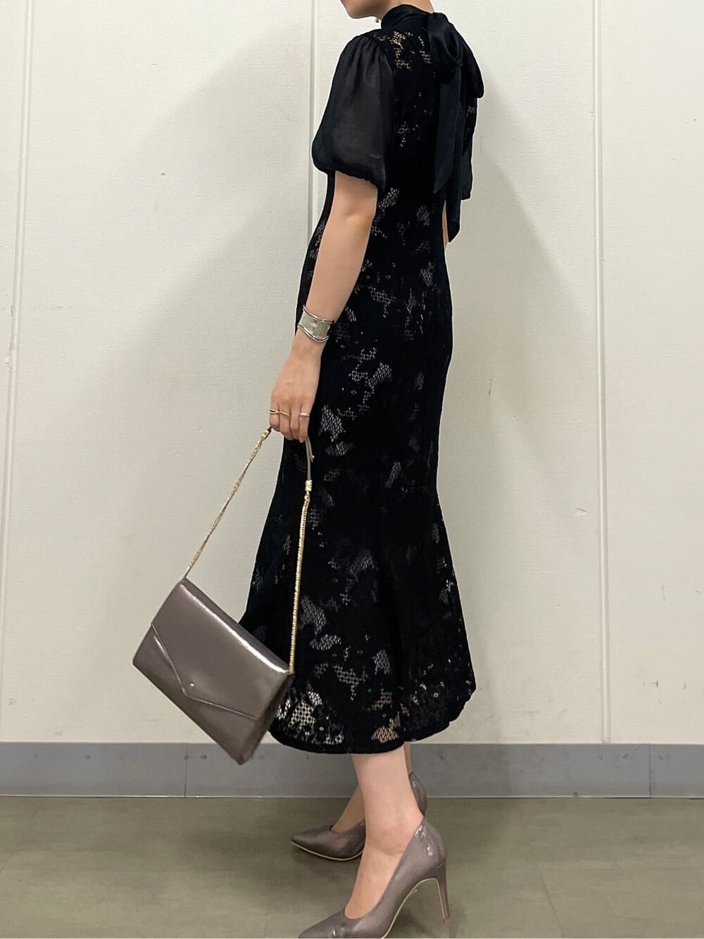 シルバー系のクラッチバッグ、シルバー系のパンプス、ブラック系のドレスを着用したレディースの夏コーディネートの5枚目の写真