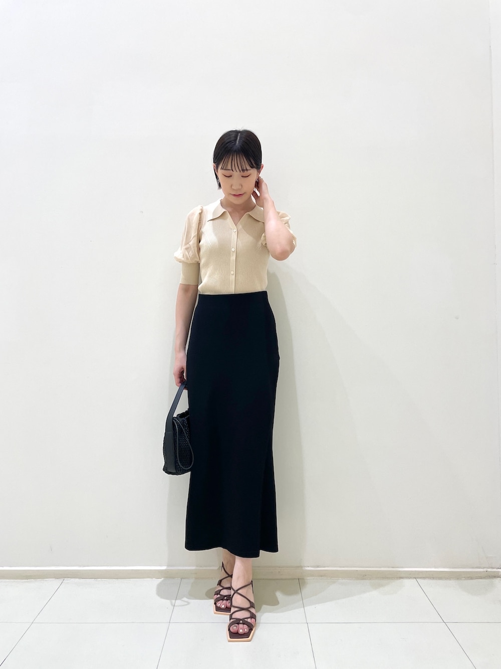 ブラック系のスカート、ホワイト系のニット/セーター、ブラック系のハンドバッグを着用したレディースの夏コーディネートの3枚目の写真
