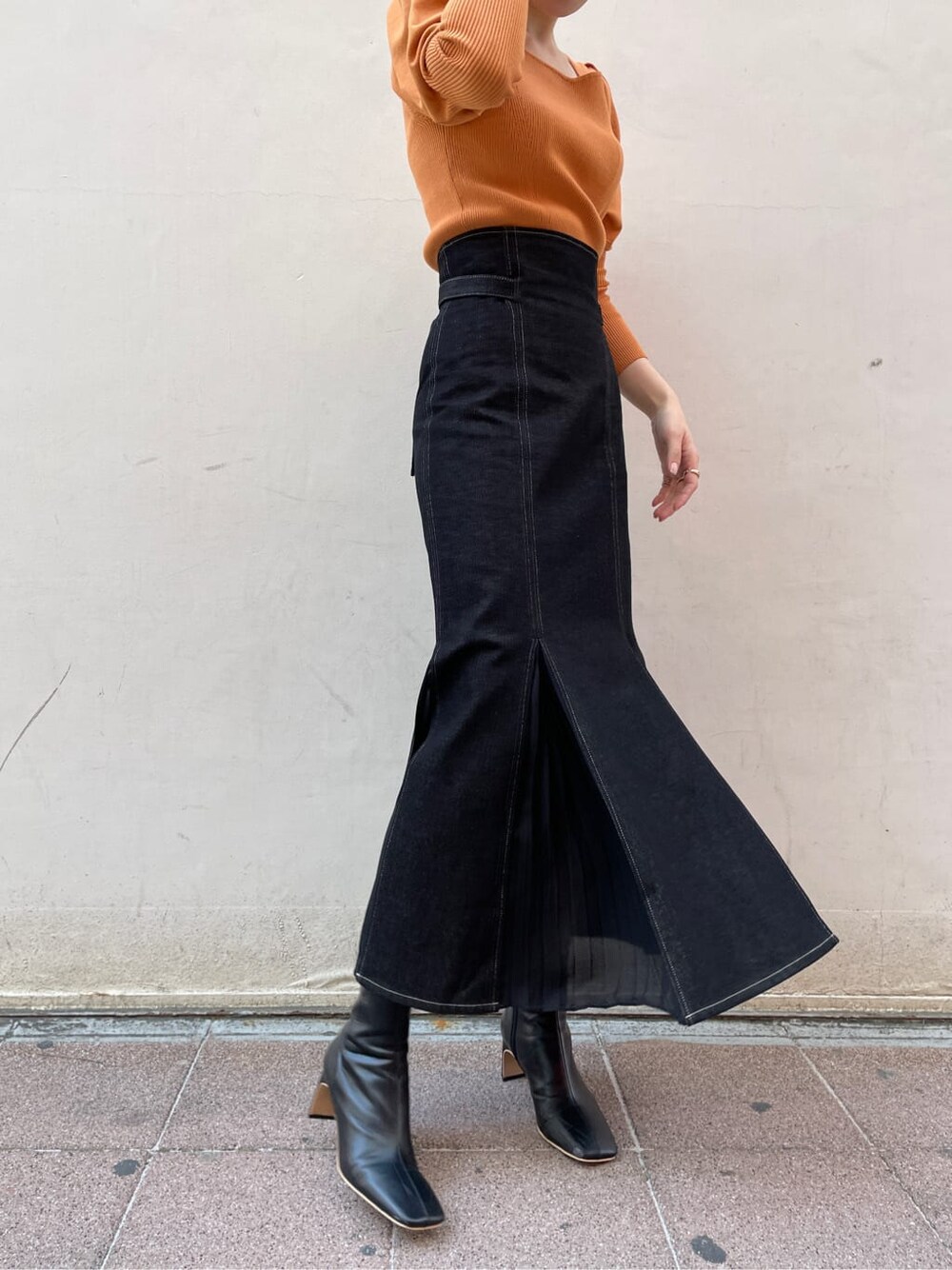 ブラック系のその他シューズ、オレンジ系のニット/セーター、ブラック系のスカートを着用したレディースの冬コーディネートの2枚目の写真