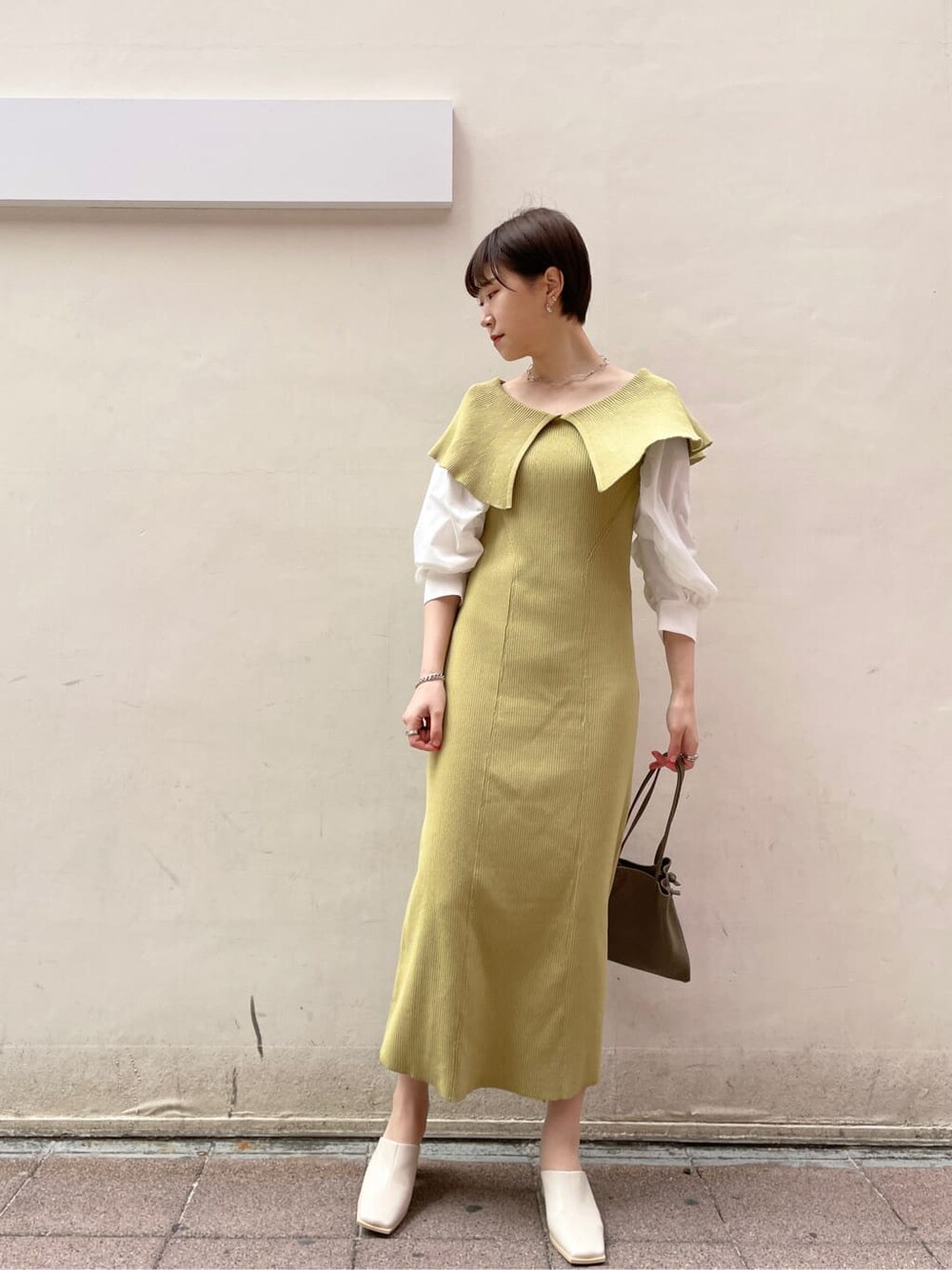 ベージュ系のハンドバッグ、ベージュ系のトレンチコート、イエロー系のワンピースを着用したレディースの冬コーディネートの2枚目の写真