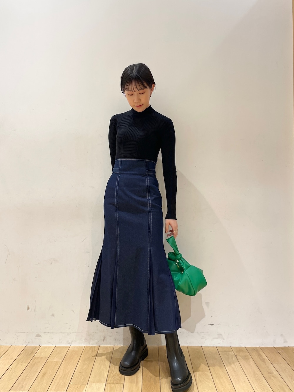 ブルー系のスカート、ブラック系のニット/セーター、グリーン系のハンドバッグを着用したレディースの冬コーディネートの2枚目の写真