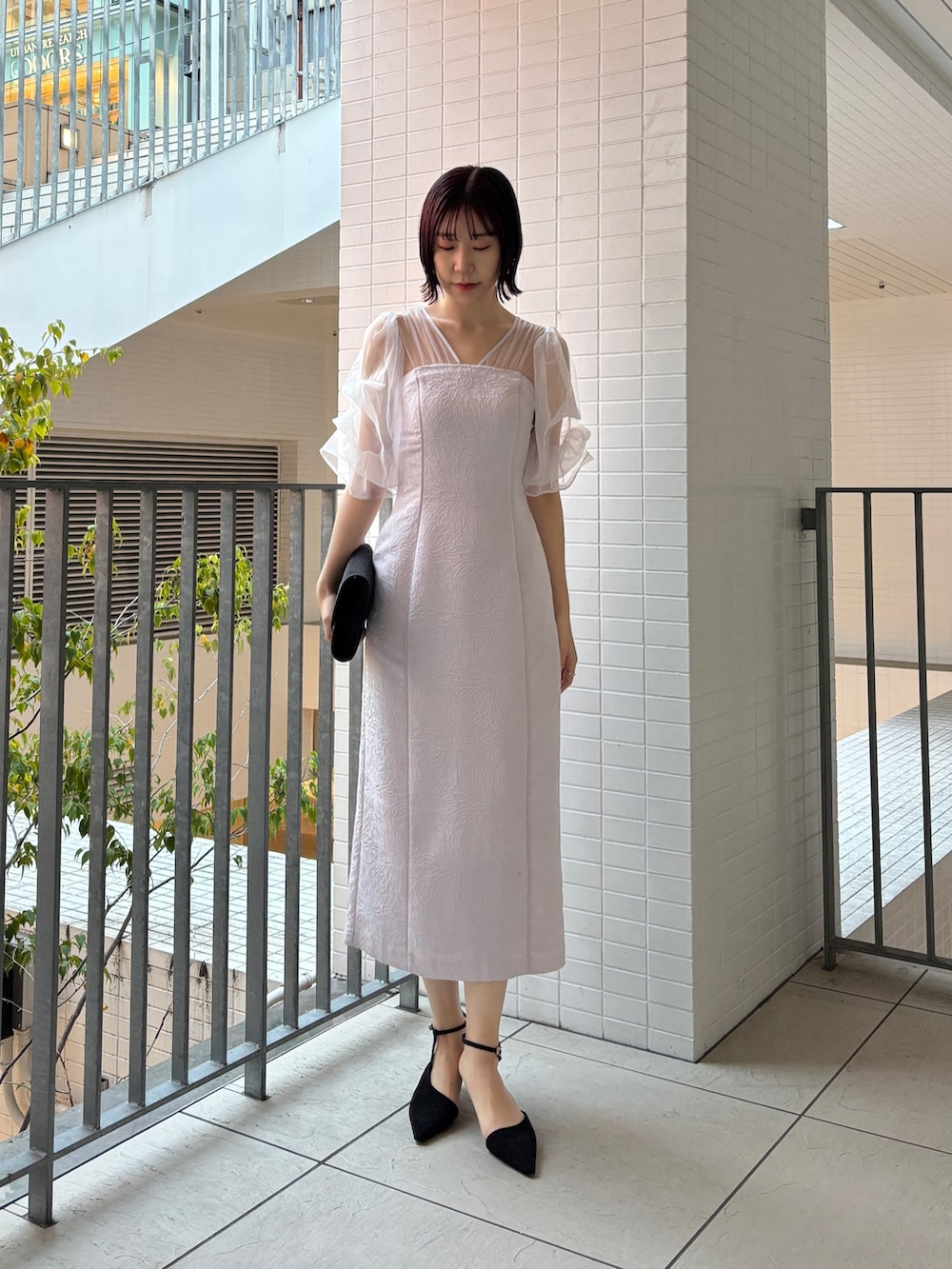 パープル系のドレス、ブラック系のハンドバッグ、ブラック系のパンプスを着用したレディースの冬コーディネートの2枚目の写真