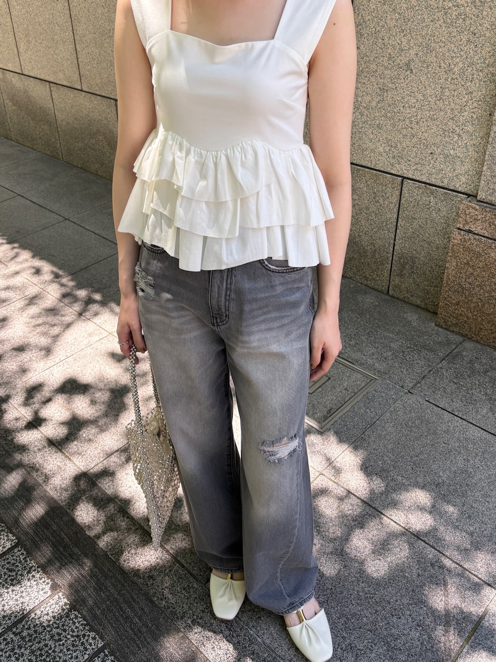 グレー系のデニムパンツ、ホワイト系のハンドバッグ、ホワイト系のサンダルを着用したレディースの春コーディネートの4枚目の写真