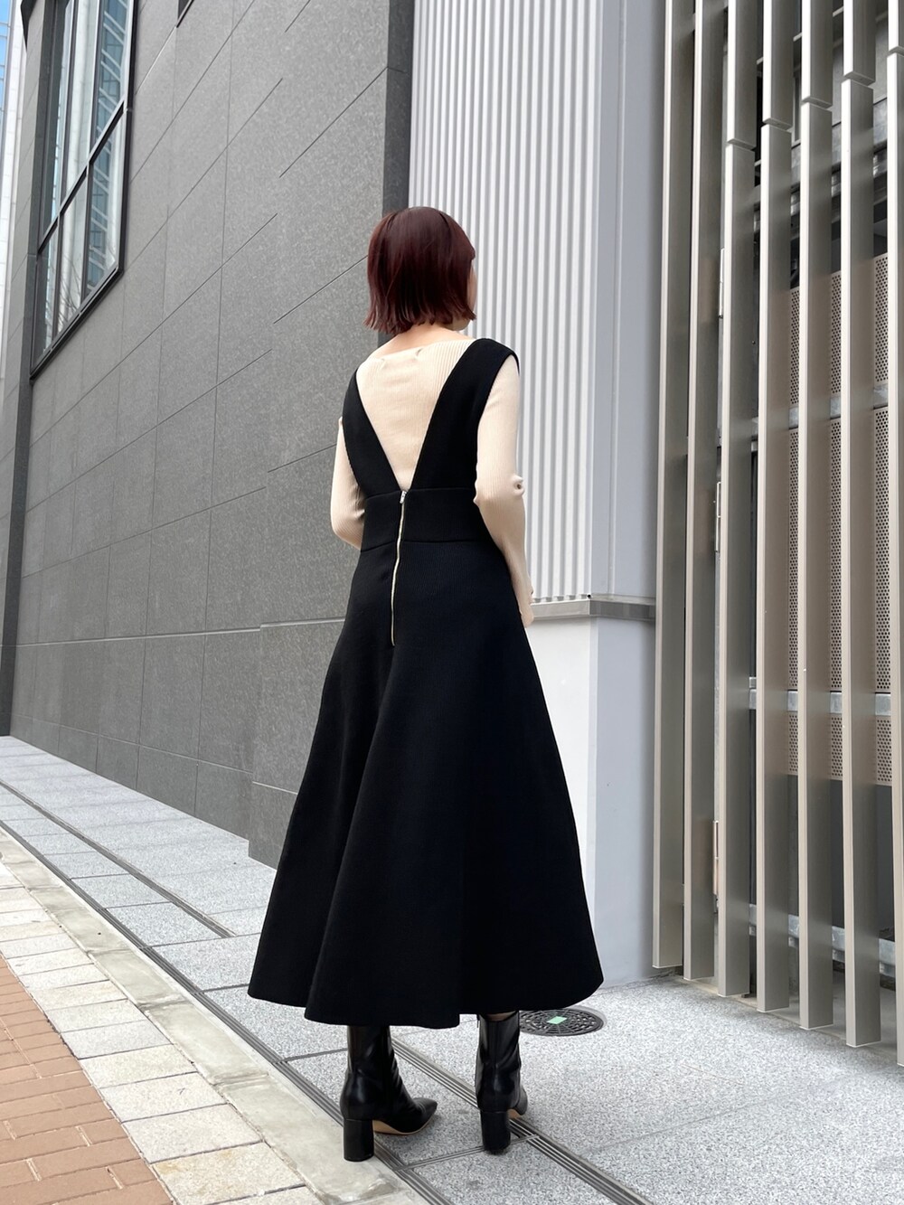 ホワイト系のニット/セーター、ブラック系のジャンパースカート、ブラック系のブーツを着用したレディースの冬コーディネートの3枚目の写真