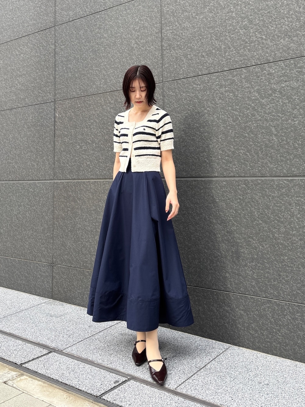 ブルー系のスカート、ホワイト系のニット/セーター、ブラウン系のハンドバッグを着用したレディースの春コーディネートの2枚目の写真