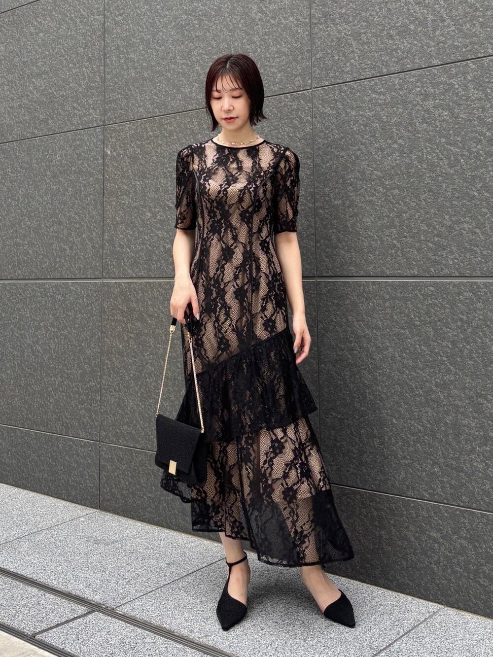 ブラック系のドレス、ブラック系のクラッチバッグ、ブラック系のパンプスを着用したレディースの秋コーディネートの2枚目の写真