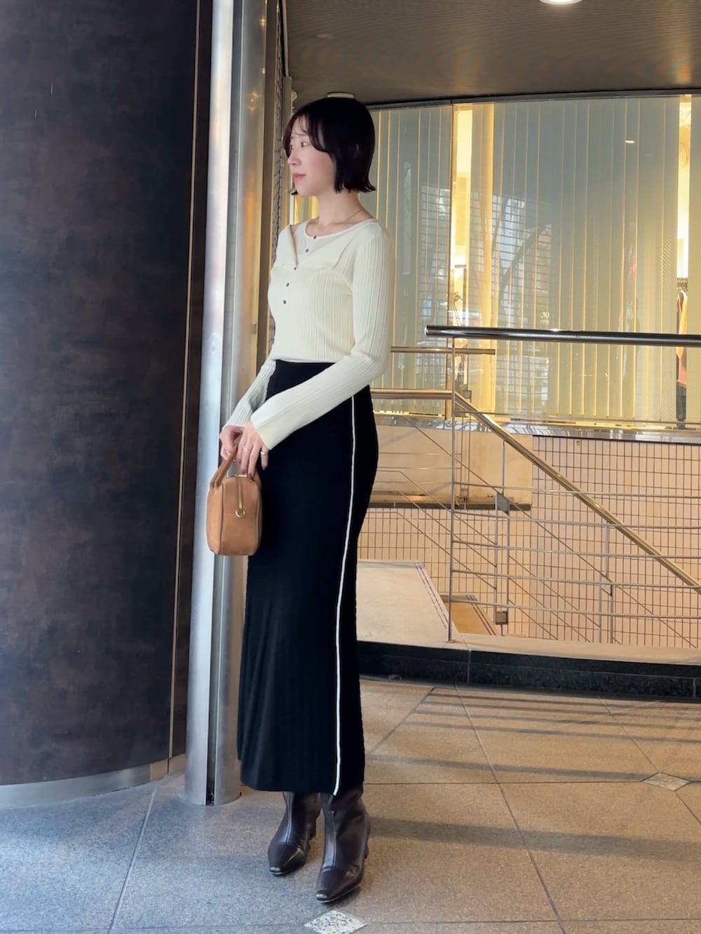 イエロー系のハンドバッグ、ブラウン系のブーツ、ホワイト系のニット/セーターを着用したレディースの冬コーディネートの2枚目の写真