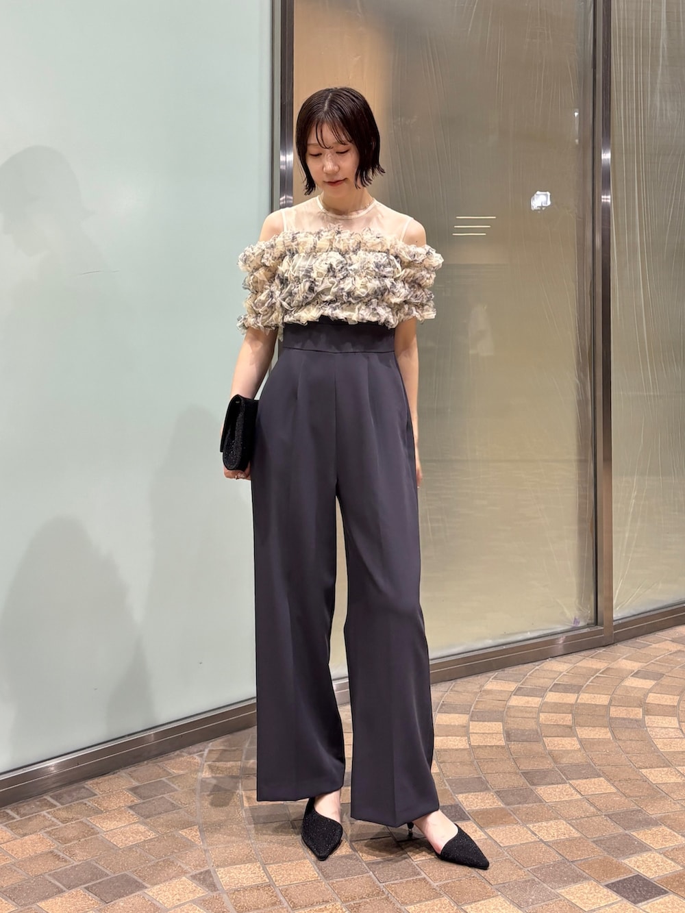 グレー系のパンツドレス、ブラック系のクラッチバッグ、ブラック系のパンプスを着用したレディースの夏コーディネートの2枚目の写真